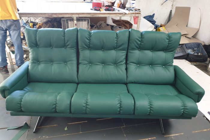 Sofá de tres plazas recién tapizado en polipiel verde con respaldo capitoné, en el taller